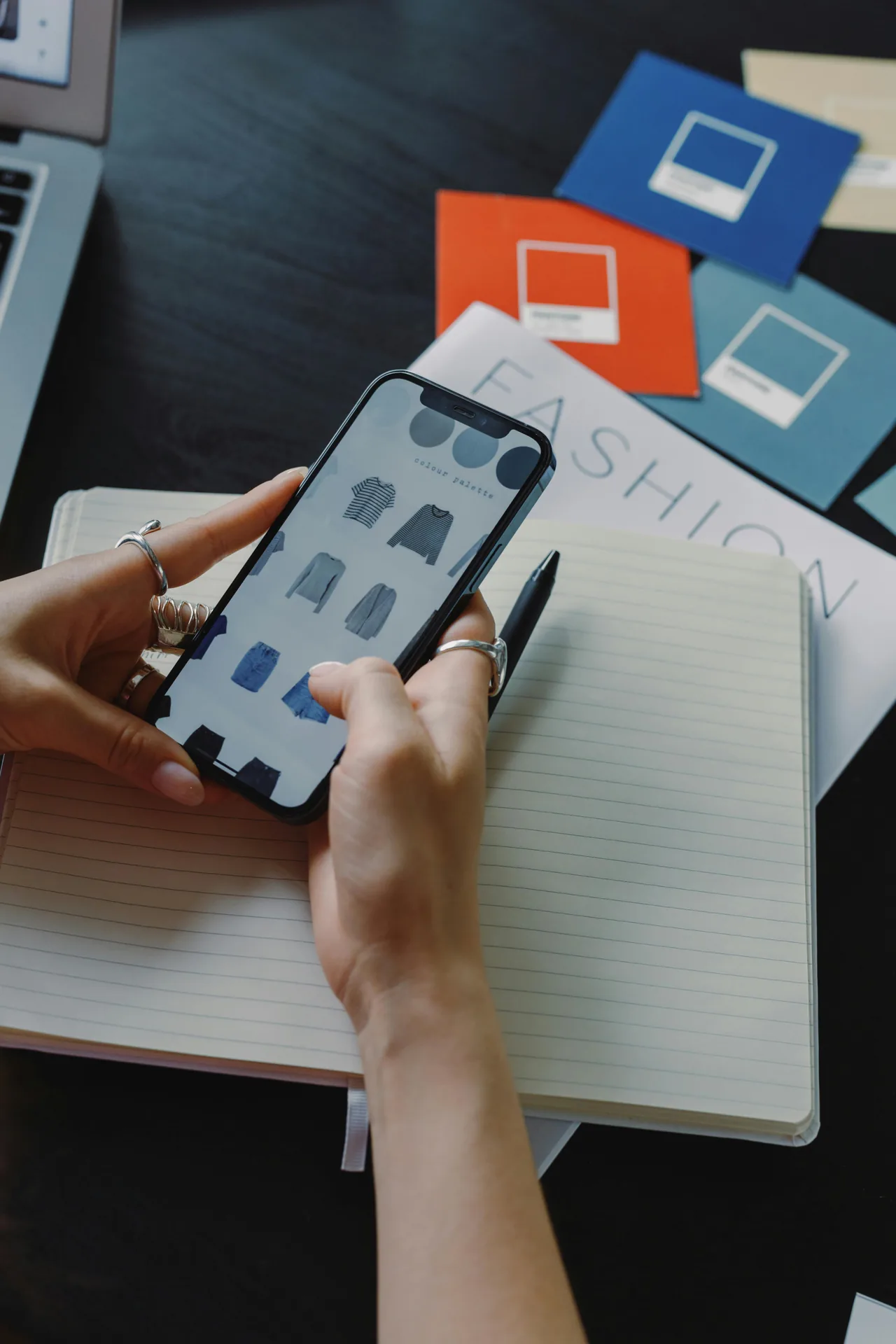 A phone showing a fashion app beside a notebook and fabric swatches