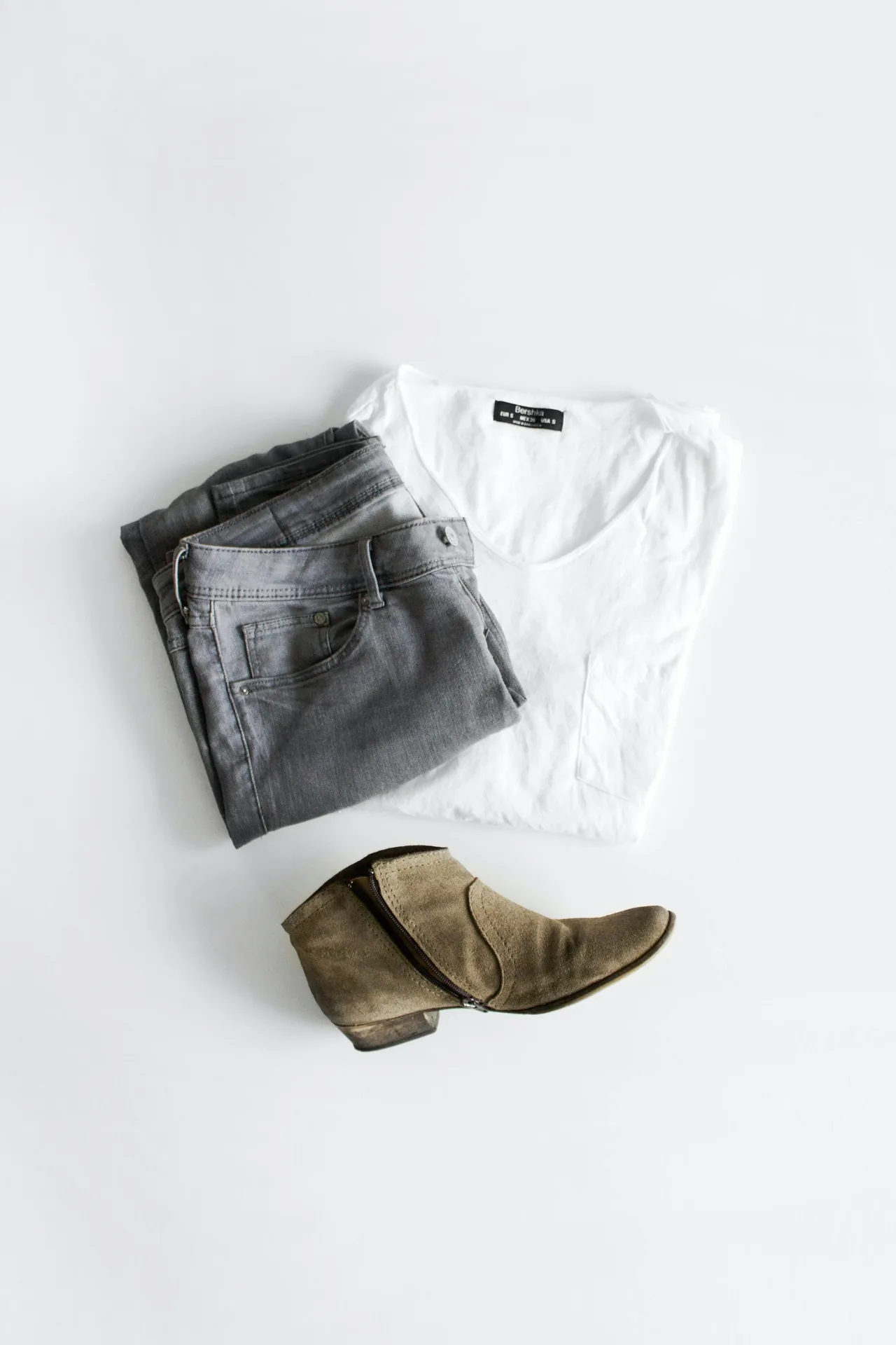 A flat-lay of a white tee, grey jeans, and ankle boots