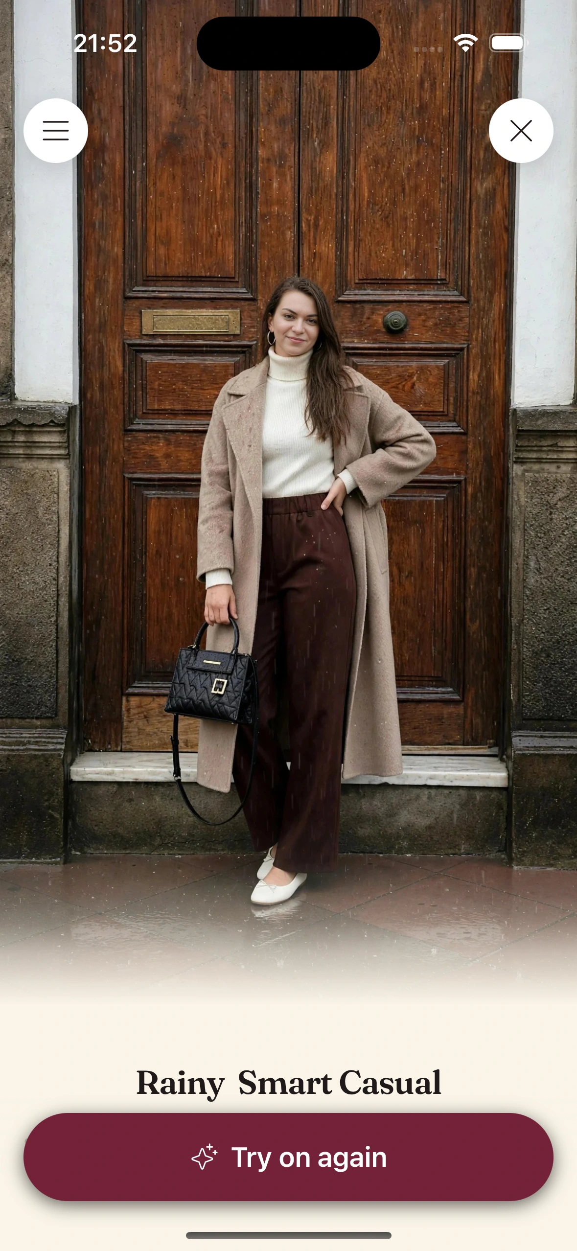A virtual try-on render for a rainy day: a long camel wool coat over a cream turtleneck, dark brown wide-leg trousers, white ballet flats and a black quilted bag, in front of a wooden door in the rain